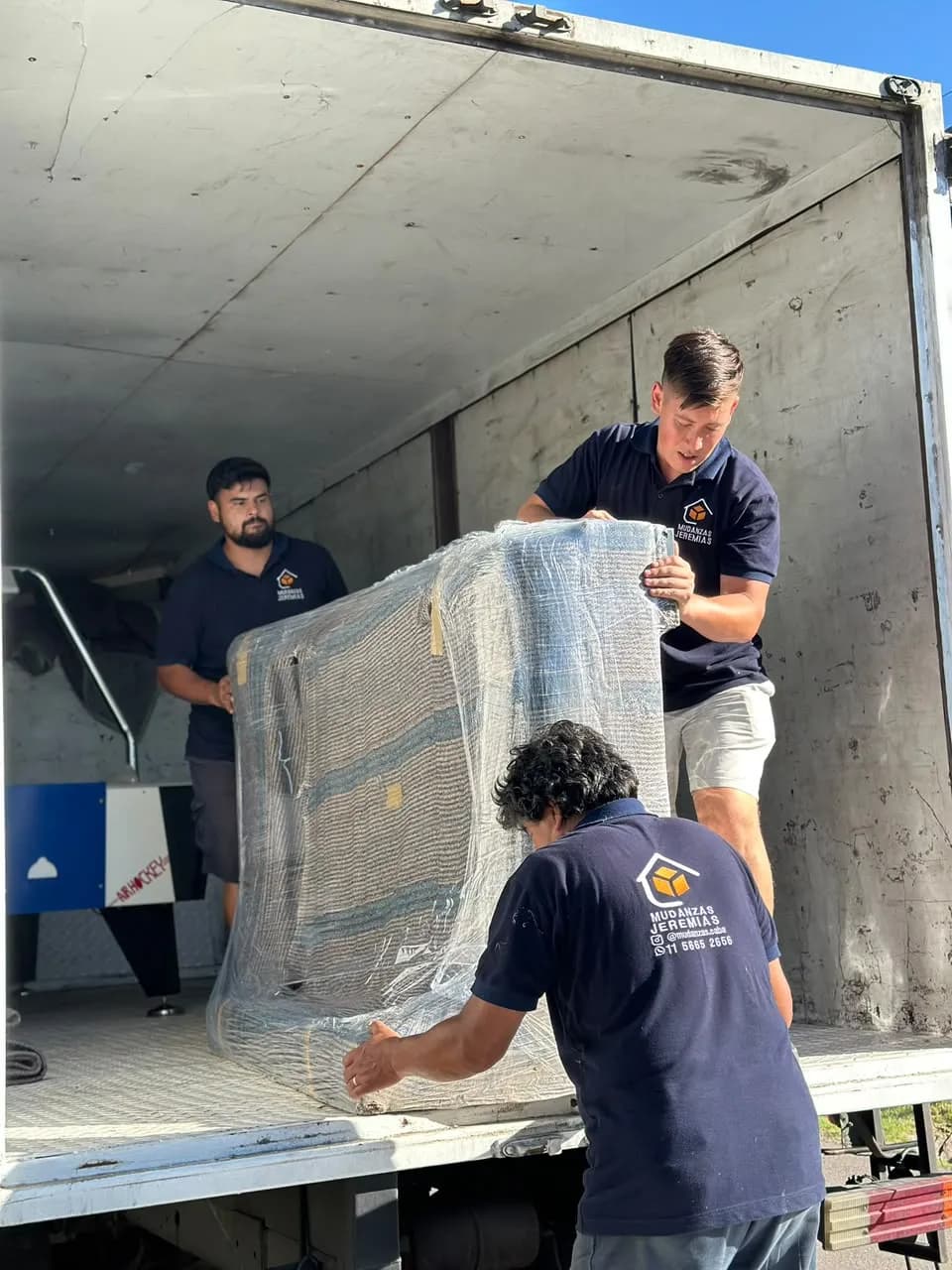 Tres integrantes del equipo de Mudanzas Jeremías cargando al camión un mueble envuelto en film y mantas